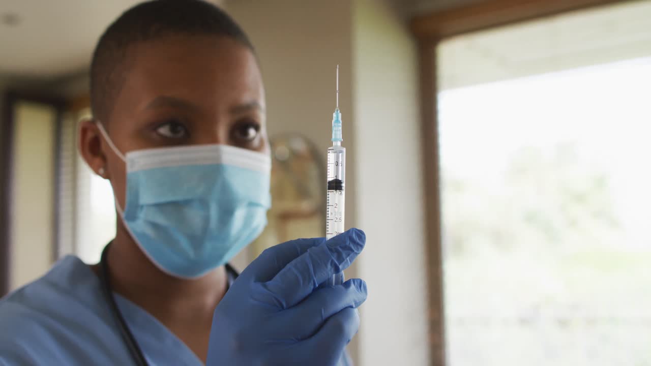 African american female doctor wearing face mask preparing covid vaccine for patient