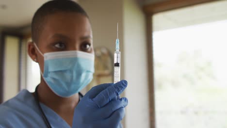 african american female doctor wearing face mask preparing covid vaccine for patient