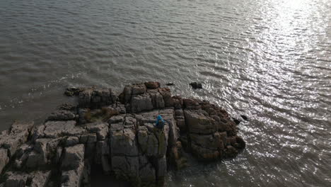 Low-angle-slow-motion-flyover-of-hiker-on-rocky-outcrop-into-murky-sea-water-at-Jenny-Brown's-Point-Silverdale-UK