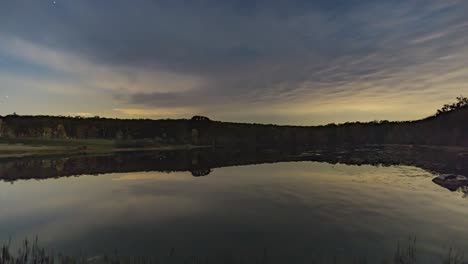 time lapse of stars and clouds over a pond with reflections