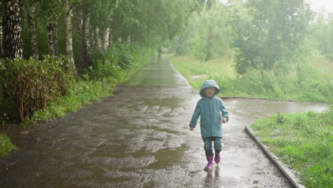 smiling boy runs across puddle in park positive little child in coat plays with water on rainy