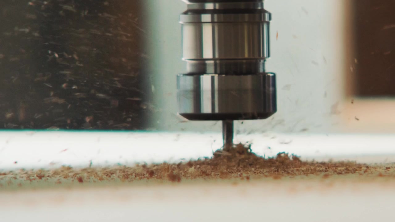 Macro primo piano al rallentatore di una punta da trapano CNC che tocca un pannello di legno durante un taglio preciso in un'officina professionale.