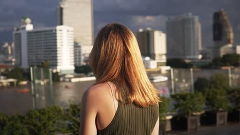 una mujer joven con cabello castaño mira el impresionante horizonte de bangkok en un día despejado