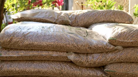 Hombre-Recogiendo-Una-Pesada-Bolsa-De-Pellets-De-Madera-De-Un-Montón-De-Bolsas-De-Pellets,-Para-Almacenarla-Durante-El-Invierno