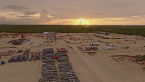 aerial drone flight over construction site field and green scenery with golden sunset in background - power plant project on dominican republic