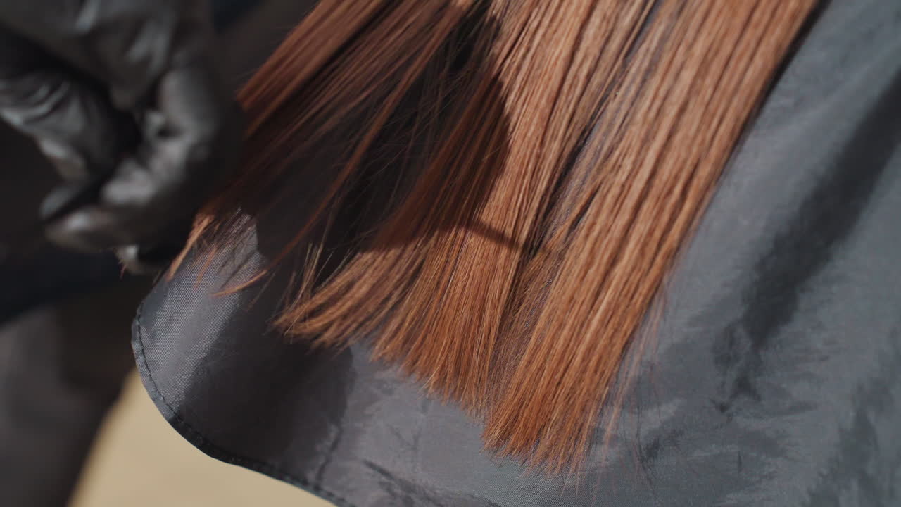 Un estilista profesional corta las puntas abiertas; un peluquero caucásico corta meticulosamente las puntas abiertas con herramientas, con un primer plano que captura al estilista recortando cuidadosamente las puntas abiertas en suaves mechones de cabello castaño