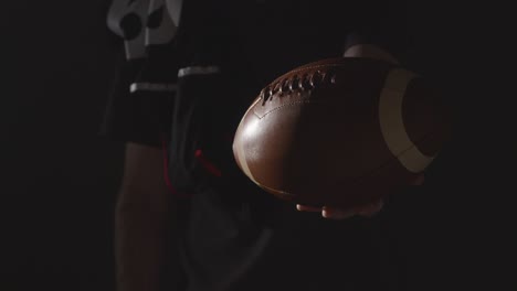 close up studio shot of american football player holding out ball with low key lighting