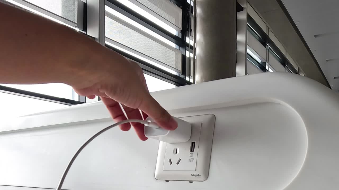 A person's hand connects a white power adapter into a modern wall outlet indoors