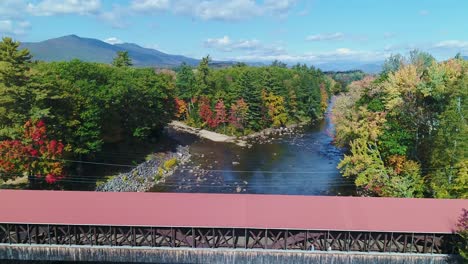 sunny rising shot of covered bridge in the fall with people to reveal mountains