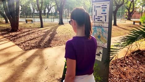 vista trasera de una joven con cola de caballo caminando tranquilamente por un parque en una ciudad