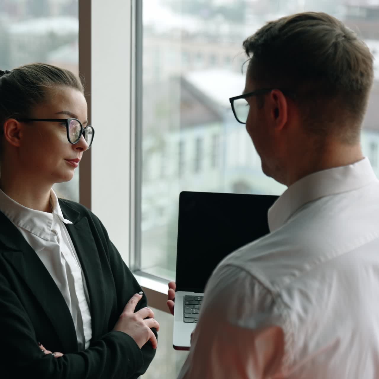 Diverse gender colleagues stand at the window communicating. Man standing his back to camera holds an I-pad