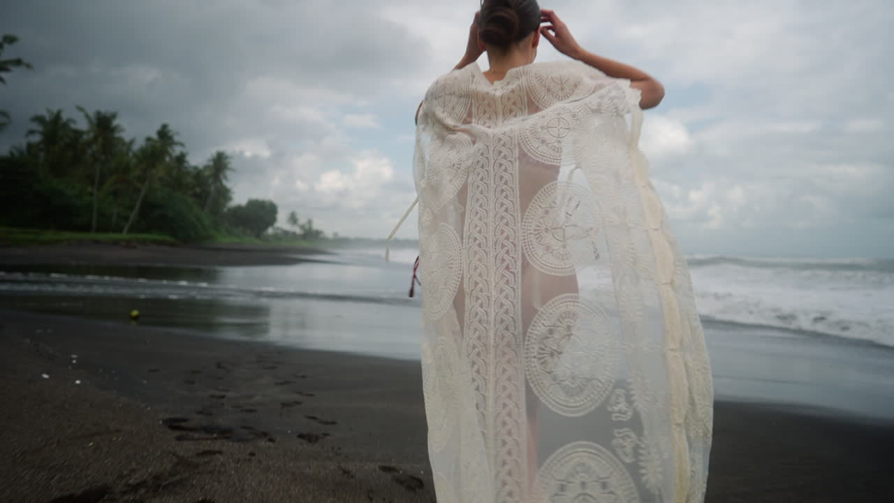 열대 지방의 변덕스러운 검은 모래 해변에서 비키니를 입은 아름답고 독립적인 여성