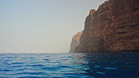 excursión por barco temprano en la mañana a lo largo de la costa rocosa volcánica de tenerife, islas canarias, españa. vista de los rayos de sol brumosos que vienen de los acantilados rocosos.