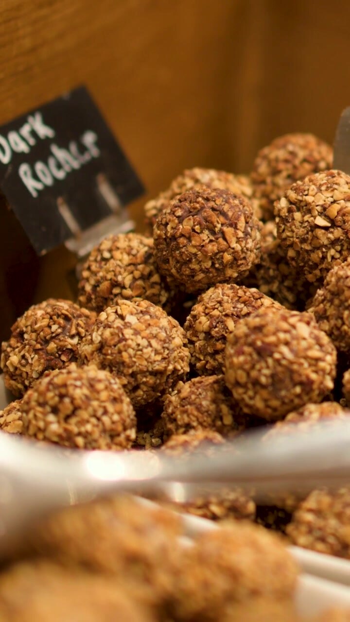 A vertical shot of gourmet nut-coated chocolate truffles arranged in a warm wooden display.