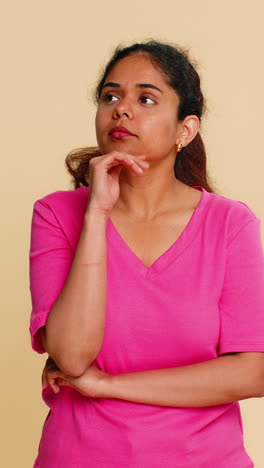 indian woman smiling thoughtfully pointing up with finger creative idea isolated on beige background