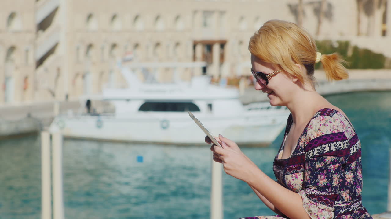 туристка наслаждается таблеткой на фоне залива с яхтами