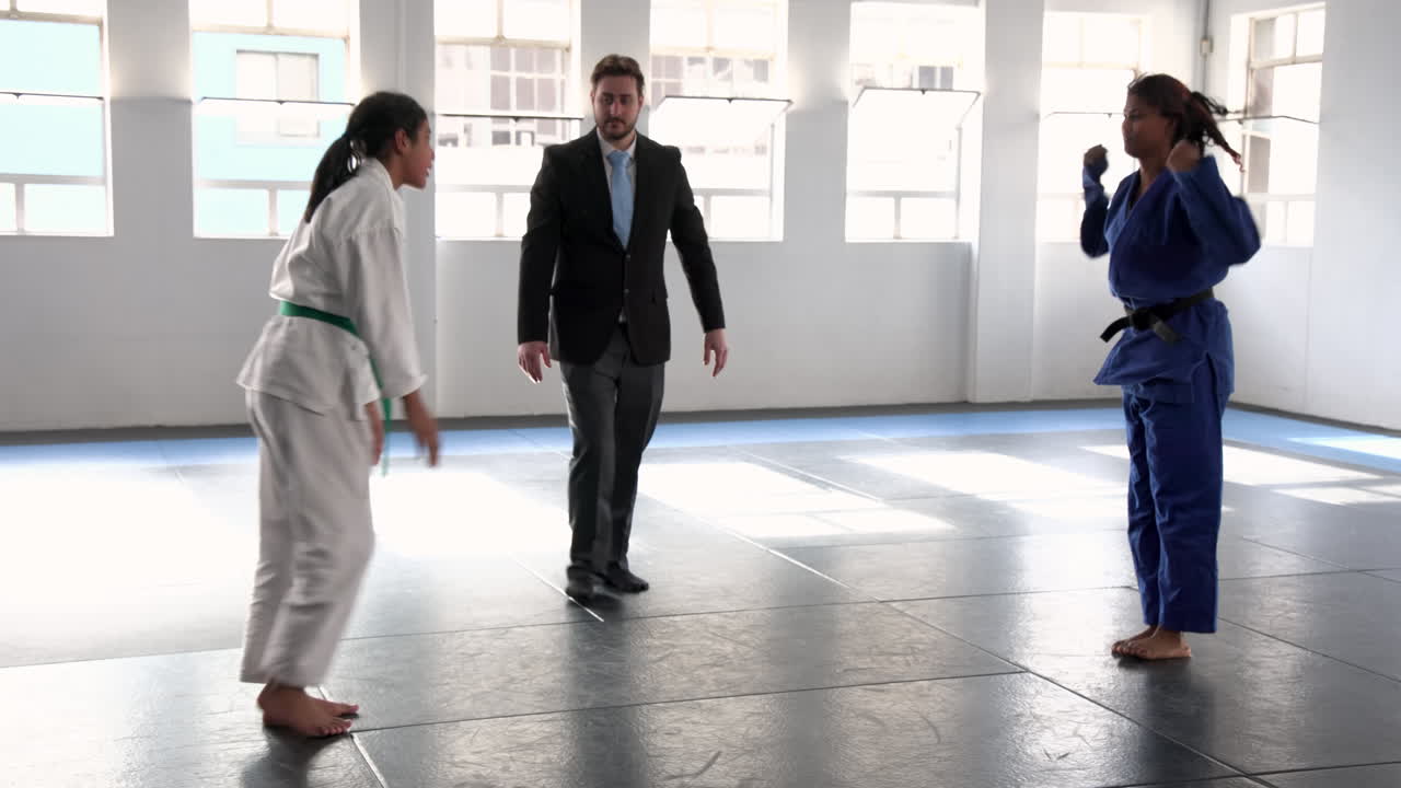 Practicing judo, two women sparring in dojo with instructor observing