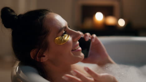 laughing model talking smartphone in bathtub closeup. happy girl laying bath