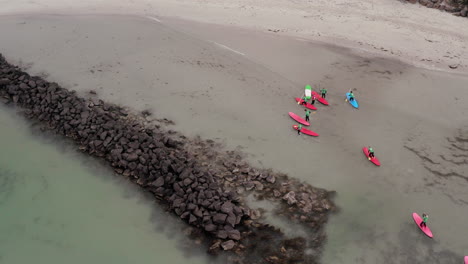 Aerial-top-down-shot-showing-group-of-sup-stand-up-paddlers-leaving-the-ocean-after-training-session