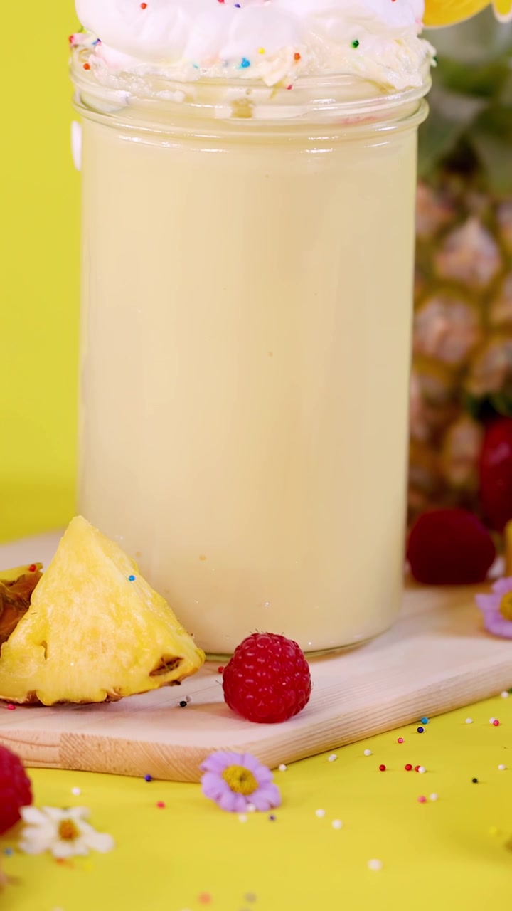 Smoothie all'ananas guarnito con panna montata, circondato da frutta, illuminazione brillante, panoramica fluida della telecamera