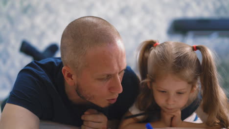 parent explains home task to daughter lying on floor in room