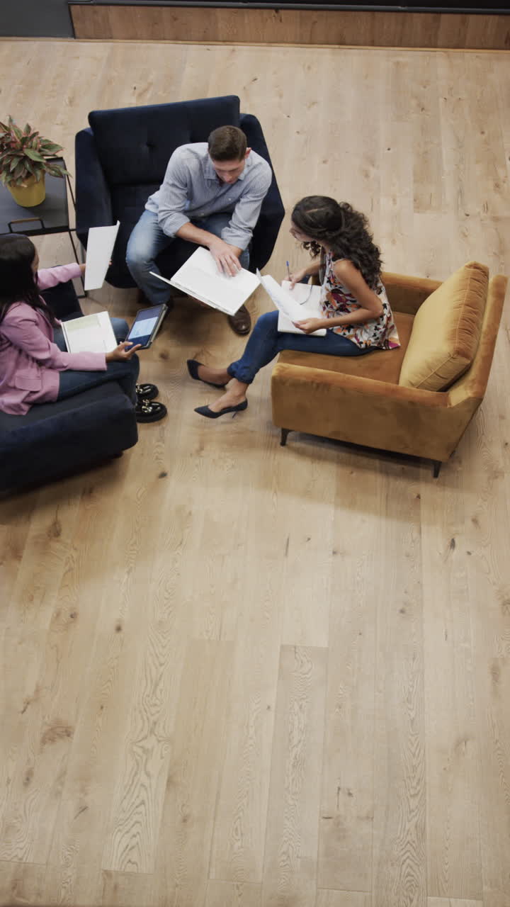Video verticale di colleghi e colleghe eterogenei che discutono usando un laptop nella sala relax dell'ufficio.