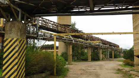 exterior view of abandoned soviet heavy metallurgy melting factory liepajas metalurgs territory, rust-covered heat pipelines on concrete poles, overcast day, wide shot