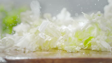 chopped chinese cabbage leaves fall onto a wet wooden table, splashing water droplets in macro and slow motion