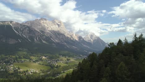 amazing aerial passing trees revealing the italian dolomites with small town in the foreground