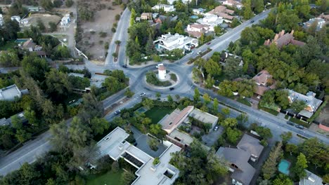 aerial dolly out rising over leonidas montes windmill in roundabout with cars driving surrounded by trees, lo barnechea, santiago, chile