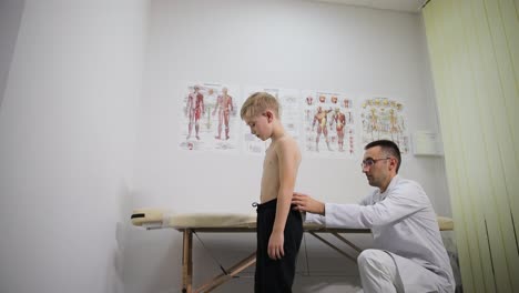 in the hospital, a doctor is assessing the feet of a young boy while he sits on a wooden chair.
