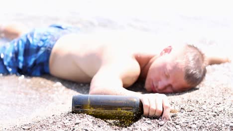 man passed out on beach with alcohol bottle