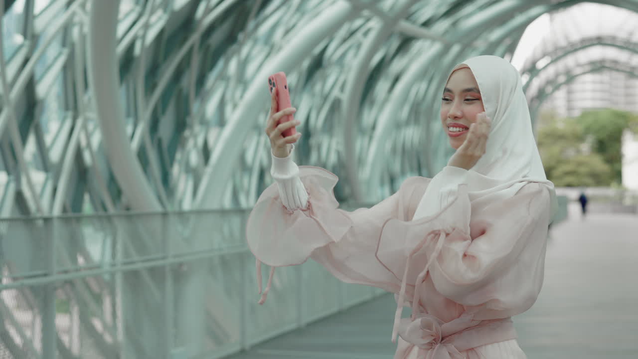 Muslim woman using smartphone on a city bridge