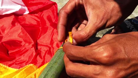 La-Mano-De-Un-Hombre-Está-Atando-Una-Cuerda-De-Bandera-En-Un-Palo-De-Bambú