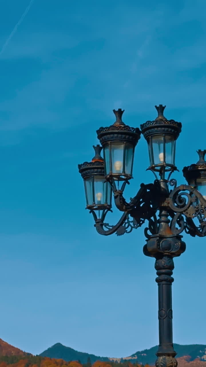 Two black street lamps of old style. Low angle view. Mountains in sunny autumn daytime at backdrop. Vertical video