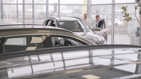 young car salesman showing to young couple new automobile at dealership salon.