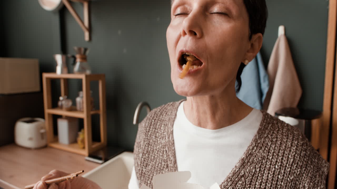 Woman enjoying takeout noodles in a kitchen