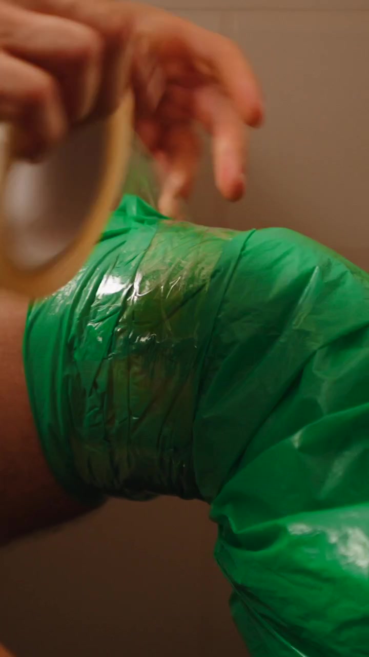 Person Securing Green Plastic Cover on Leg with Adhesive Tape