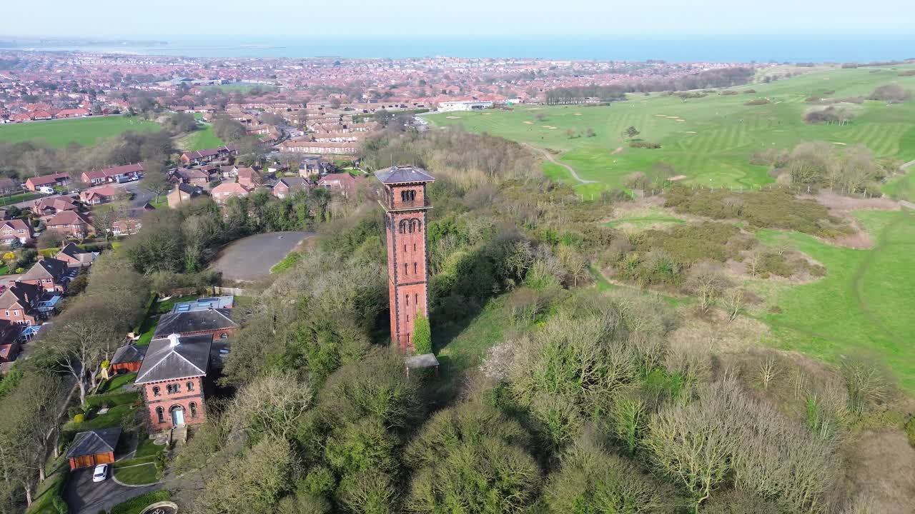 Orbita di drone sopra la Torre dell'acqua di Cleadon, un punto di riferimento storico in mattoni, i tetti del villaggio e i campi verdi a Cleadon, South Tyneside, nel nord-est dell'Inghilterra in una giornata limpida.