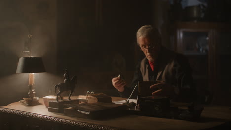 older passionate man evaluates an old watch in his office at night