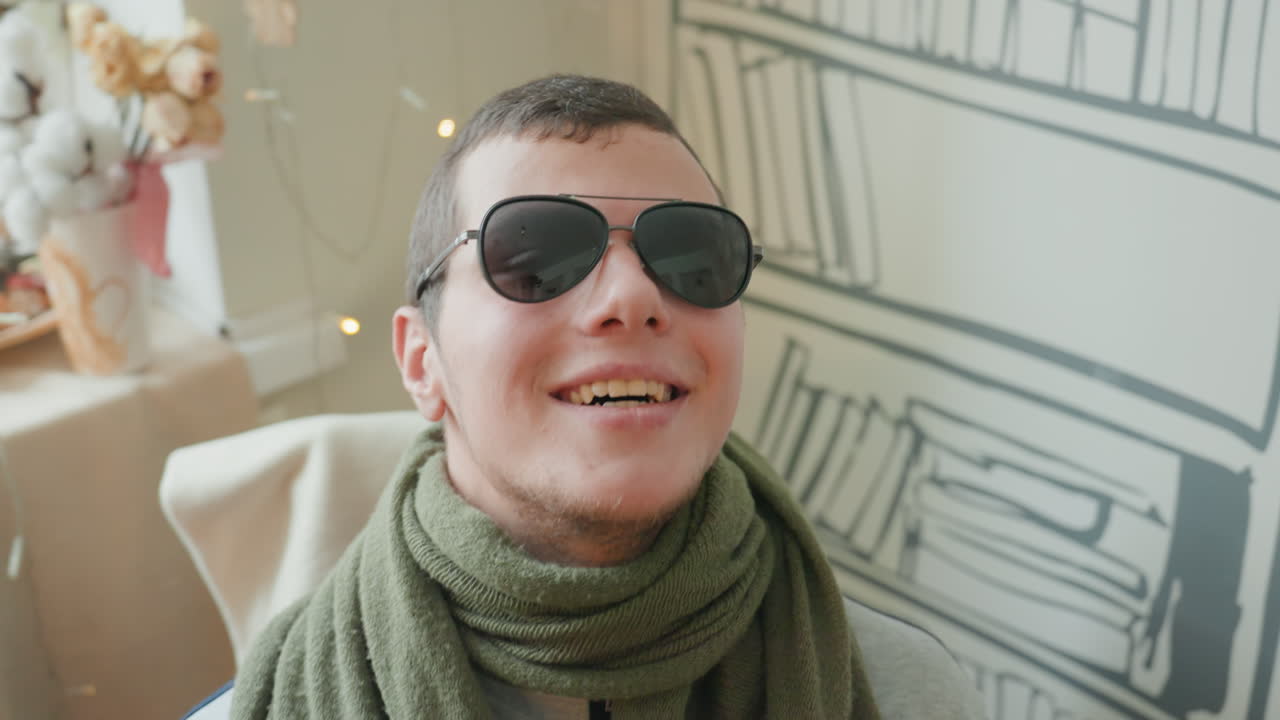 Uomo allegro con occhiali da sole tra decorazioni vivaci e fate. Individuo gioioso che indossa occhiali da sole circondato da opere d'arte vivaci e luci fatate scintillanti in un ambiente di studio colorato.