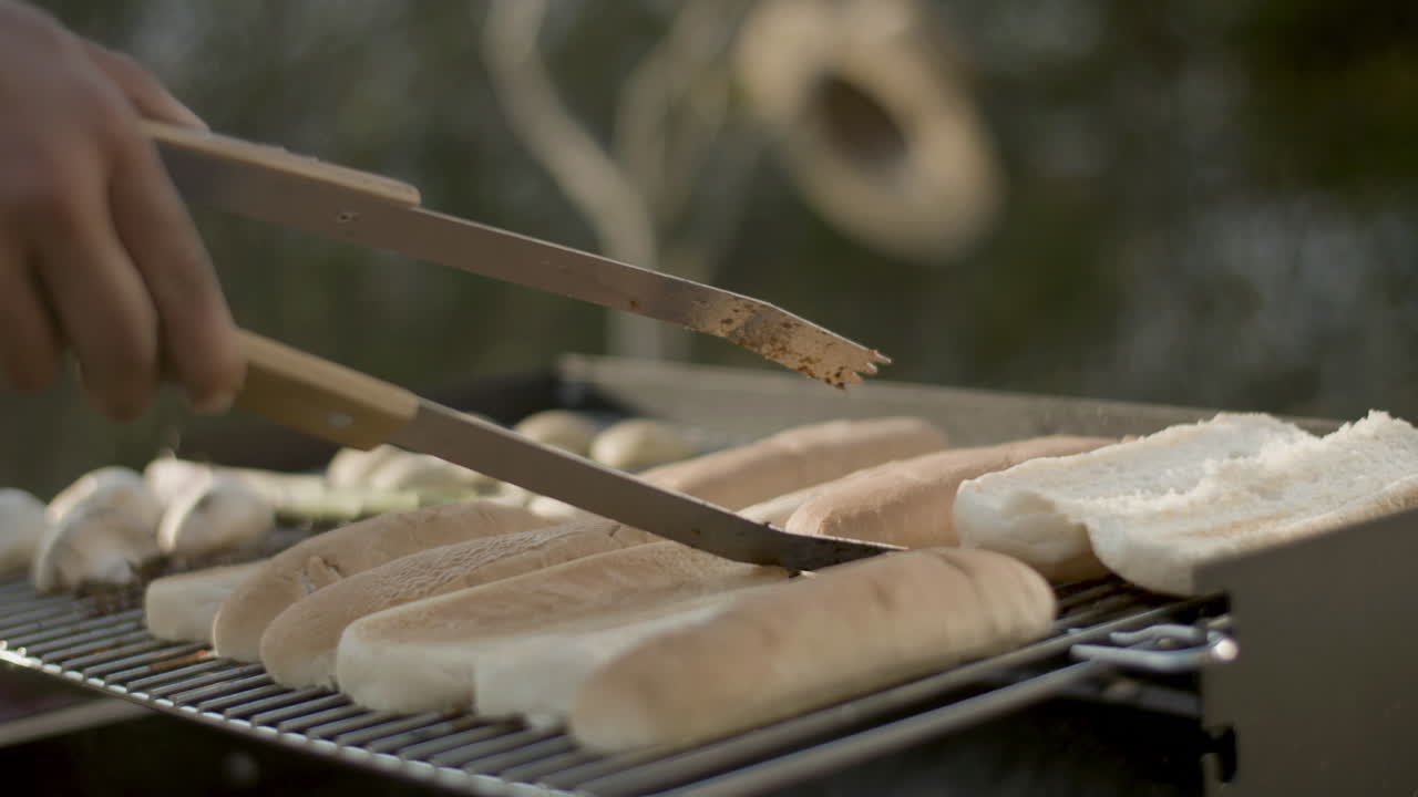 Mano maschile che mette il pane per hotdog sulla griglia del barbecue.