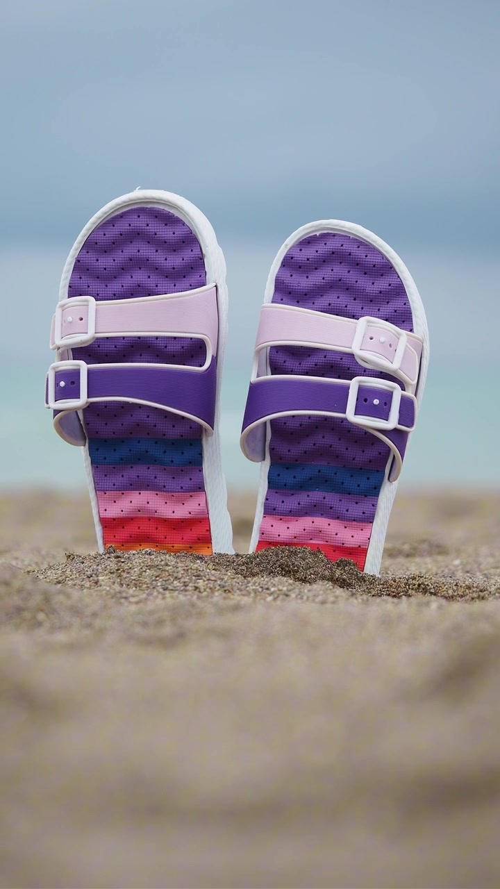 Farverige regnbuesandaler på en sandstrand ved havet