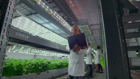 microbiology in white coats go on a modern farm with laptops and tablets studying the results of tests and collecting samples for the study of new species of plants. combating climate change and creating sustainable plants.