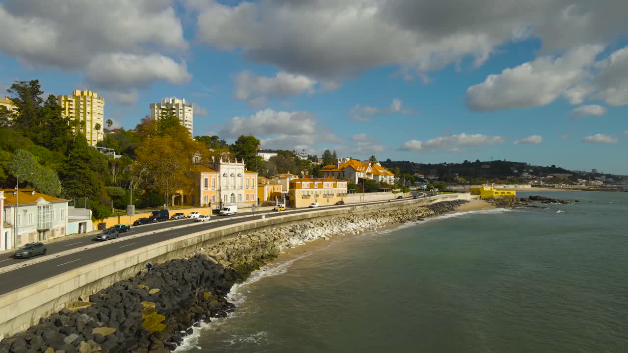 Ampia ripresa aerea orbitale lungo la costa di Caxias e Paço de Arcos con il fiume Tago, che rivela le tradizionali ville costiere portoghesi, il verde, il traffico in movimento e l'oceano sotto nuvole spettacolari vicino a Lisbona