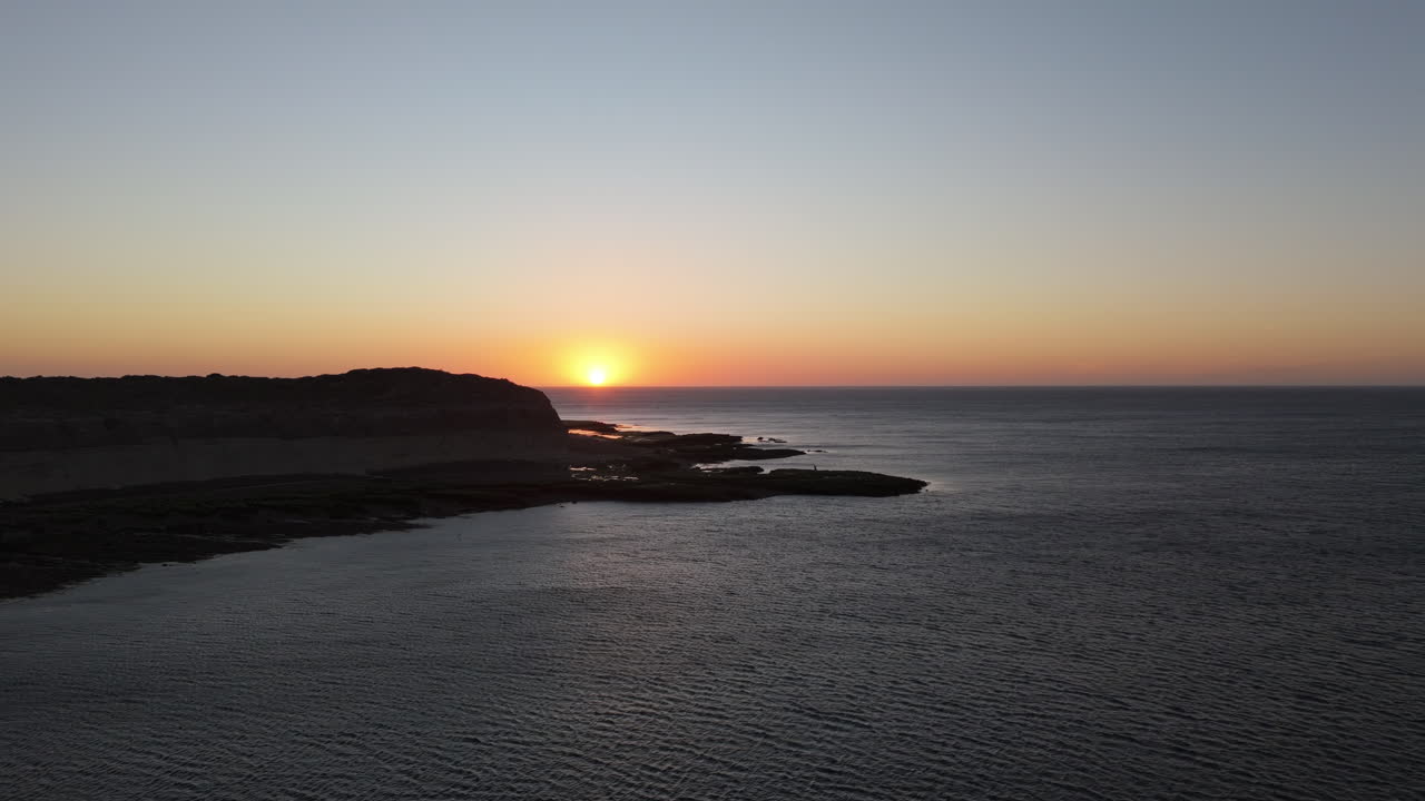 Imagens aéreas sobre o oceano de Puerto Madryn ao nascer do sol, com tonalidade vibrante do céu, falésias e península. Horizonte distante. Filmado em 4K 60fps.