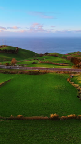 highways built around the picturesque green meadows on the rocky landscape. waterscape at backdrop. the azores. top view. vertical video.