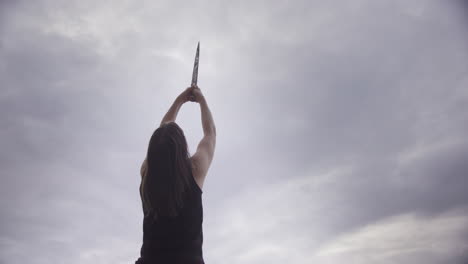 empowered woman with bare arms holds sword up to sky, female power