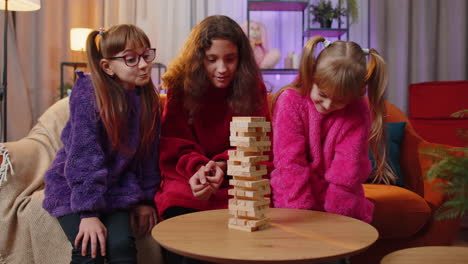 Three-siblings-children-girls-playing-with-blocks-board-game,-build-tower-from-wooden-bricks-at-home