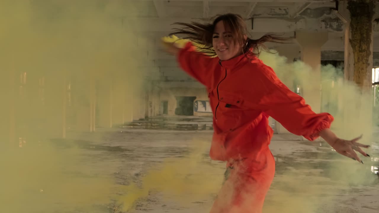 mujer joven con ropa naranja bailando con humo amarillo en las manos. bailarín de hip hop
